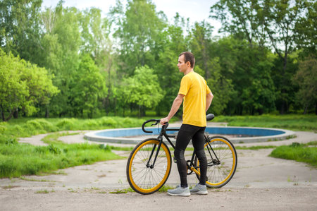 A young Man stopped to rest With his Bicycle in a public Park. He enjoys an early Sunny morning in...