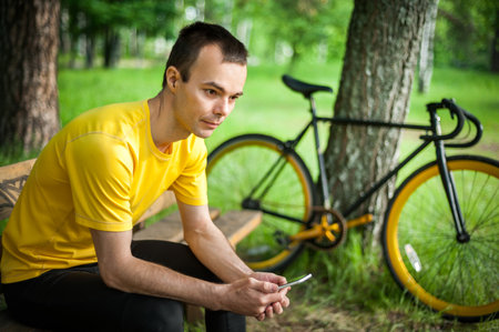 A young man sitting on a bench in a public Park communicates via mobile communication. In the...