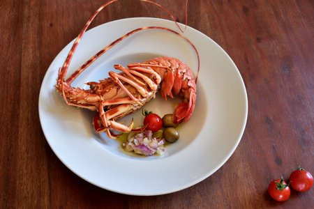 A boiled lobster lies in a white plate with side dishes on a rustic wooden table as a backgroundの写真素材