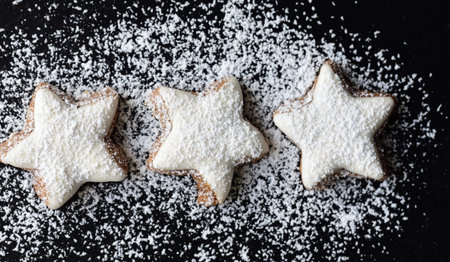 Fresh biscuits in the form of stars with white frosting and powdered sugar against dark background