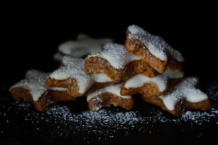 Fresh biscuits in the form of stars with white frosting and powdered sugar against dark backgroundの写真素材