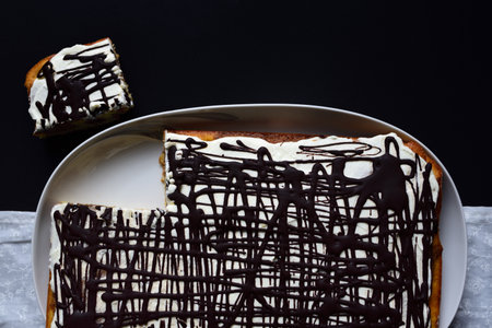 A cake with cream and chocolate photographed from above with a cut piece against a dark backgroundの写真素材