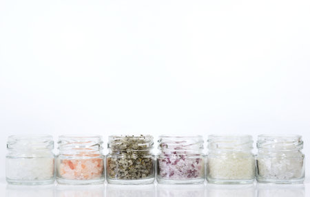 Several jars filled with different types of salt stand side by side against a white background with space for textの写真素材