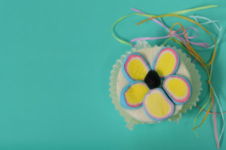 A small, colorful cupcace made of sugar lies against a colorful background as a close-up for an invitation, photographed from above, with space for textの写真素材