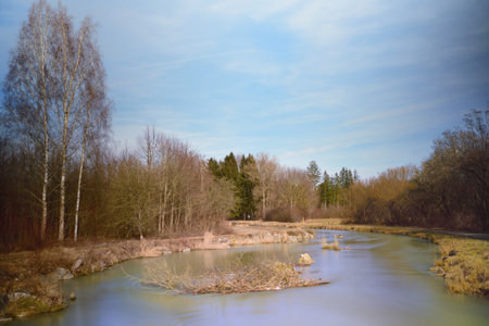 Long shot of a landscape with a small calm river that flows calmly in the winter in front of barren...