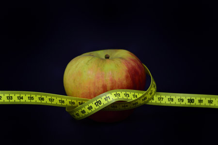 A fresh red apple wrapped in a yellow tape measure against a dark background with space for text