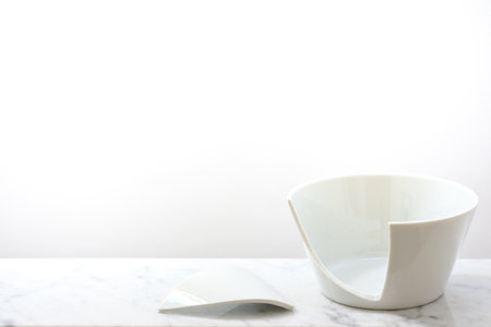 A broken white ceramic bowl stands against a white background on a light marble plate with space for textの写真素材