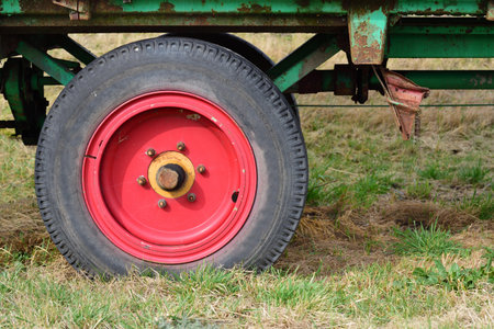 Detail of an old agricultural vehicle, with a red old wheel and tires, on a meadowの写真素材