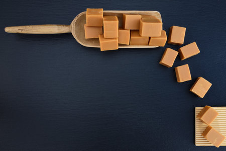 Background of a black slate blackboard with a wooden scoop of caramel in cubes and caramel cubes next to itの写真素材