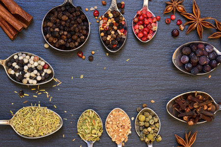 Many different spoons with different spices form a frame in front of a slate of slate