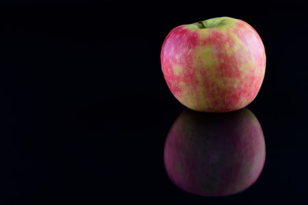 A fresh healthy apple is reflected against a dark background