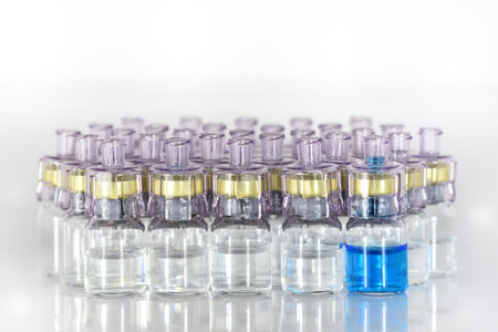 Several ampoules with a transparent liquid, medicine or vaccine stand against a light background. One ampoule contains blue liquidの写真素材