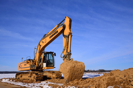 A yellow shovel excavator stands in winter near Augsburg, against a blue sky, on loamy soil. A lot...
