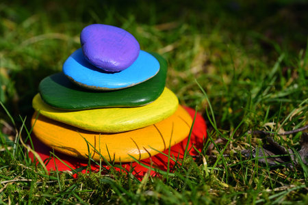 Several brightly colored pebbles painted in rainbow colors lie on top of one another in a meadow with green grassの写真素材