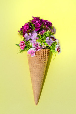 Still life with an ice cream cone, on a yellow background. In the bag there are many colorful flowers, so-called mustaches, which are in the waffle instead of the ice creamの写真素材