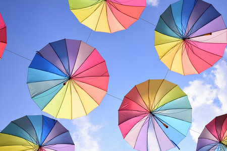 Colorful umbrellas in the colors of the rainbow hang in the air next to each other against a blue skyの写真素材
