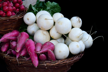 In a wicker basket, red and white radishes lie heaped on top of each other against a dark background...
