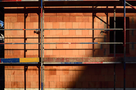 Background and detail of a freshly laid red brick wall, leaving room for a window, behind metal scaffoldingの写真素材
