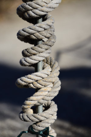 Against a dark-colored background, a thick rope made of natural fibers wrapped around a metal rod in...