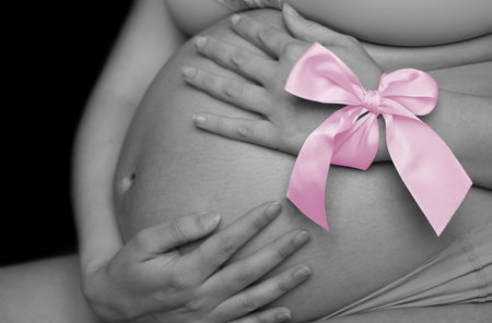 Belly of a pregnant woman from the side in black and white. The woman holds a pink bow on her handの写真素材