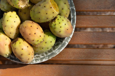 Several ripe prickly pear fruits lie in a ceramic bowl. The bowl stands on a base made of rustic wood. There is space for text.の写真素材