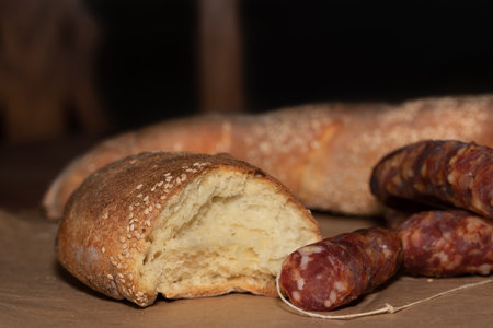 White bread with sesame seeds on it lies on a table. The bread is sliced. In front of it is dried...