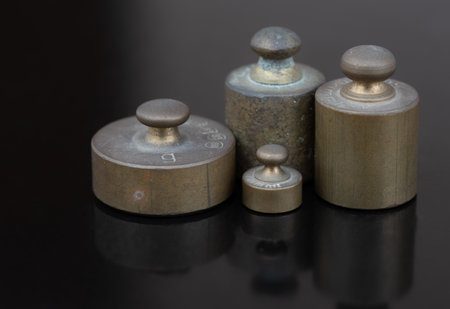 Four metal weights stand next to each other in front of a dark background and are reflected on the ground. These are small weights for a scaleの写真素材