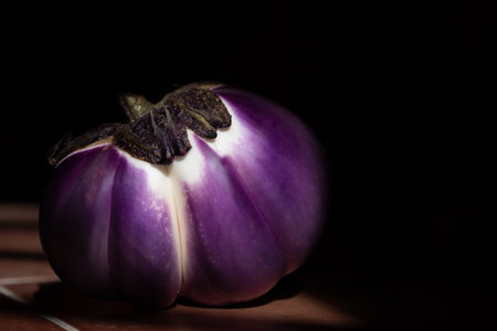 Close-up of a ripe purple eggplant against a dark background. The vegetables lie on brown tilesの写真素材