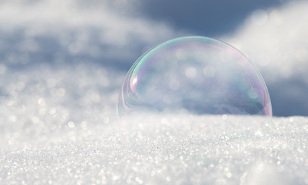 A shimmering soap bubble lies on light-colored snow. The light shines on the bubble in winterの写真素材