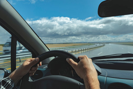 Windscreen view of nature, road, sky and hand of man on the steering wheel in a spring, summer or...