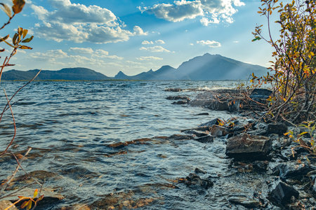 Lake with stone shore against background of mountains and blue sky. Landscape with lake and...