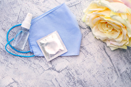 Protective medical mask, rose, condom and sanitizer on a white textured background. The concept of love relationships in a new normal reality. Preparing for date. Copy space, flat layの写真素材