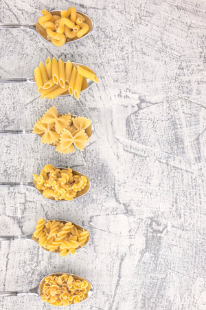 Italian foods concept and menu design. Various kind of Pasta Farfalle, Pasta A Riso, Orecchiette Pugliesi, Gnocco Sardo and Farfalle in spoons setup on white stone background with flat lay.の写真素材