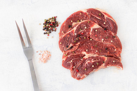 Raw beef meat with spices on a white stone background. Beef near the fork. Top view.の写真素材