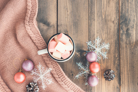 Cup with hot coffee with foam and marshmallows on of wooden table, wrapped in warm knit woolen scarf near snowflakes.The concept of winter, warmth, holidays and events.Soft focus.Top viewの写真素材