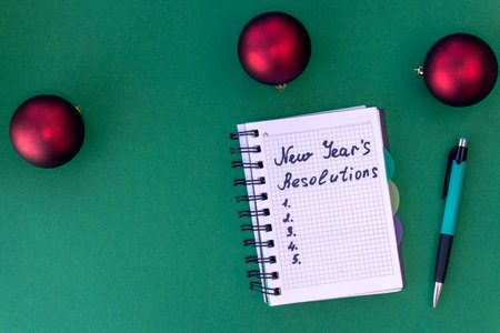 New Year's resolutions concept. Writing in a notebook New Year's resolutions on green background with Christmas balls. Flat lay. Top viewの写真素材