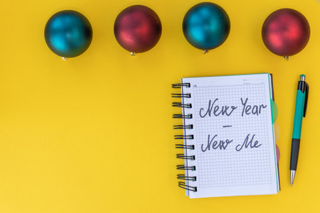 New year - new me. Inspiration concept. Writing in a notebook New year - new me on yellow background with Christmas balls. Top view. Flat layの写真素材