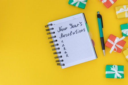 Writing in a notebook New Year's resolutions on yellow background with Christmas gifts. New Year's resolutions concept. Flat lay. Top viewの写真素材
