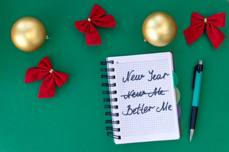 Writing in a notebook New Year - better me on green background with Christmas balls and bows. New Year's resolutions concept. Flat lay. Top viewの写真素材