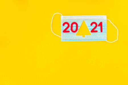Medical mask with cut-out silhouette of Christmas tree and red numbers 2021 on yellow background.New...