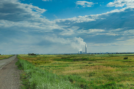 Smoking chimneys of plant in green field on backgrounds of blue sky. Environmental pollution concept. Human influence on nature.の写真素材