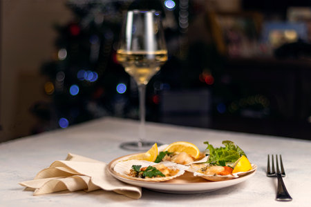 Baked scallops with caviar in a plate against the background of blurred glasses of wine. Scallops with lemon on a black background with a napkin and a fork. Soft focusの写真素材