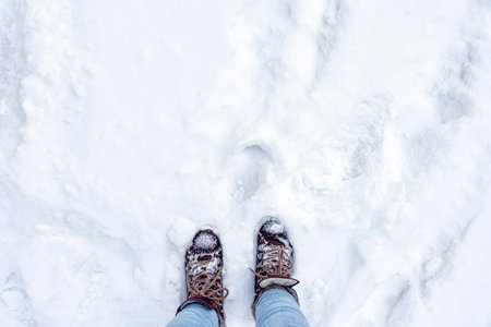 Legs in burgundy boots and blue jeans in the snow. Footprints in the snow. Winter landscape. Soft...