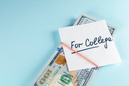 Text written note FOR COLLEGE with dollars cash money in rubber band, on copy space blue background...