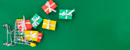 Banner with fallen small cart with scattered gifts. Red, green and yellow gifts in a shopping...