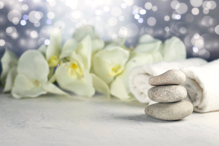 Spa resort therapy composition with massage stones, rolled towels, and orchid flowers, abstract lights. Concept of spa, relax or resort. Soft focusの写真素材