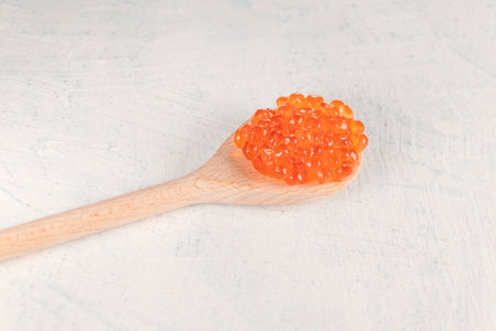 Delicious, crumbly, big red caviar in a wooden spoon on a white background. Soft focusの写真素材