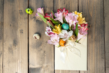 Bouquet from pink, yellow, magenta, white and red alstroemerias and painted quail eggs in holiday envelope with bow. Happy Easter concept. Soft focusの写真素材