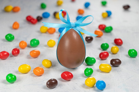 big chocolate egg with a blue bow on a white concrete background with colorful little eggs. Concept...