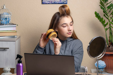 A teenage girl with curlers looks at the mirror. beautiful teenage girl doing her hair in front of the laptop.の写真素材